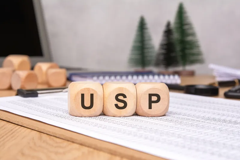 Wooden letter blocks spelling USP resting on a printed spreadsheet on a desk